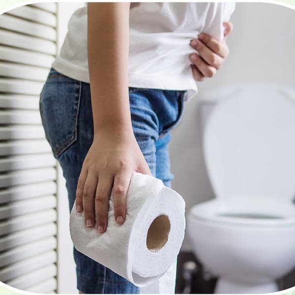 Orang berdiri di samping kloset, satu tangan memegang perut, tangan lain memegang tisu toilet